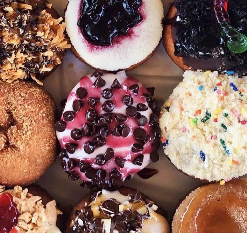 Overhead view of Peace, Love & Little Donuts decorated donuts with coconut, blueberry, chocolate chip, cookie crumb, and sprinkle toppings