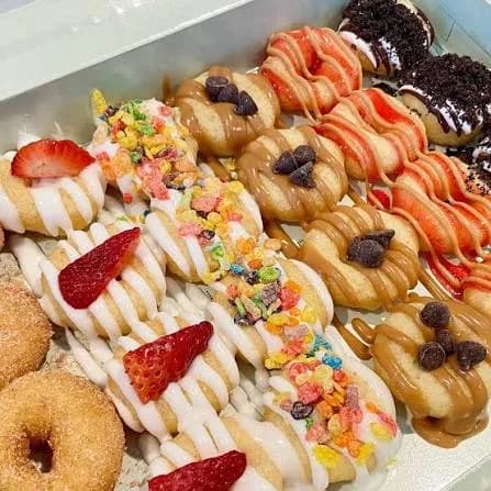 Box of The Dapper Doughnut mini doughnuts topped with strawberries, fruity cereal, chocolate chips, red drizzle, cookie crumbles, and cinnamon sugar