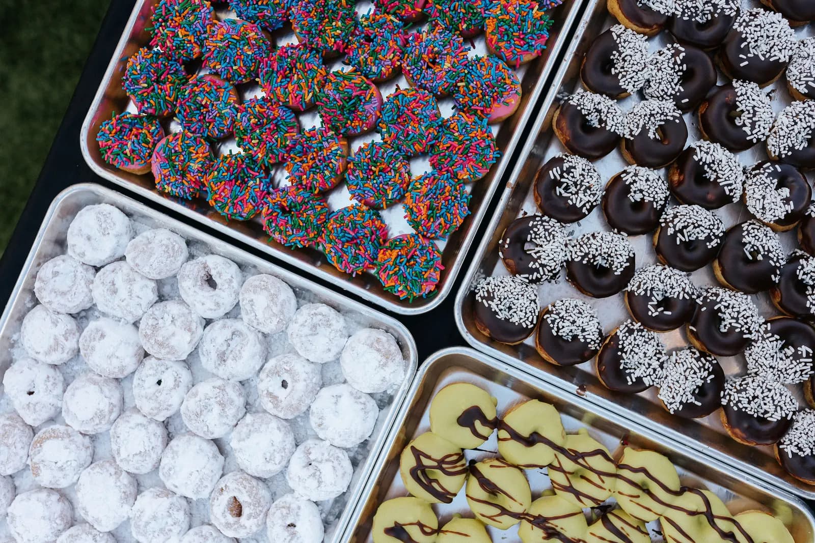 Four trays of frosted mini donuts outdoors